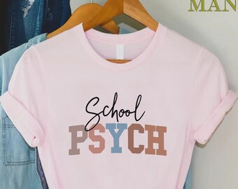 May include: Pink t-shirt with the text "School PSYCH" in colorful block letters. The text is in a casual, handwritten font.
