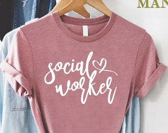 May include: A dusty rose t-shirt with the text "social worker" in white script with a small heart above the word "social".