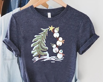 May include: A dark blue t-shirt with a graphic of snowmen climbing a Christmas tree. The snowmen are wearing hats and scarves. The tree is green with white snow on the branches.