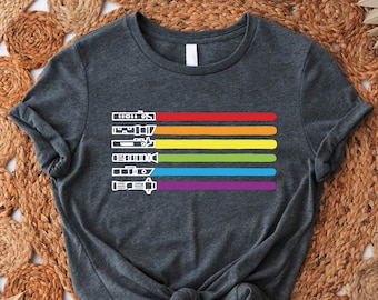 May include: A dark gray t-shirt with a rainbow pride flag design featuring a row of light saber silhouettes.