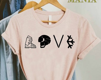 Könnte beinhalten: Ein pinkfarbenes T-Shirt mit einem schwarzen Grafikdesign, auf dem "LOVE" mit Skischuh-, Helm- und Schneeflocken-Symbolen steht.