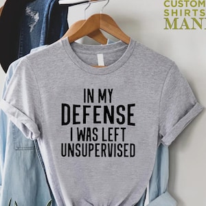 May include: Gray t-shirt with black text that reads "In my defense I was left unsupervised".