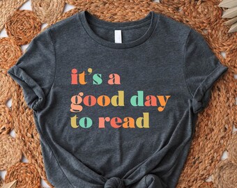 May include: A dark gray t-shirt with the text "it's a good day to read" in colorful letters. The letters are in shades of orange, yellow, green, and blue.