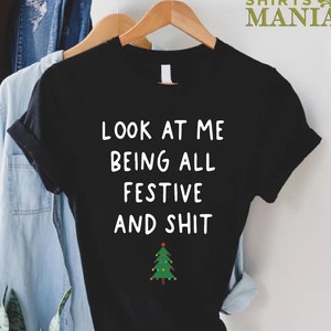 May include: Black t-shirt with white text that reads "Look at me being all festive and shit" and a green Christmas tree with lights.