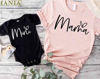 May include: A pink t-shirt with the word "Mama" and a small heart printed on it. A black t-shirt with the word "Mini" and a small heart printed on it.