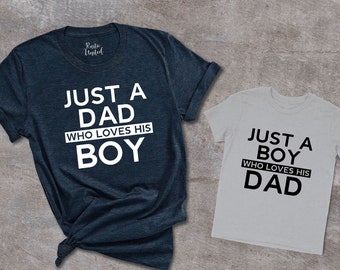 May include: Two t-shirts, one navy blue and one light gray, with matching text. The navy blue shirt says "Just a Dad who loves his Boy" and the light gray shirt says "Just a Boy who loves his Dad".