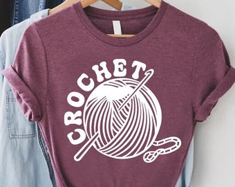 May include: A maroon t-shirt with the word "CROCHET" in white letters and a white illustration of a ball of yarn and a crochet hook.