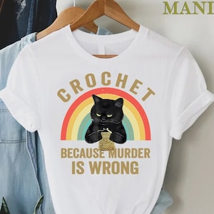May include: White t-shirt with a black cat holding yarn in front of a rainbow with the text "Crochet because murder is wrong."