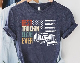 Könnte beinhalten: Ein marineblaues T-Shirt mit einer weißen Grafik eines Sattelschleppers und dem Text "Best Truckin' Dad Ever" mit einem verblassten amerikanischen Flaggen-Design.