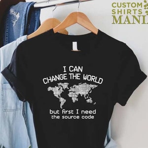 May include: Black t-shirt with a white graphic of a world map and the text "I can change the world but first I need the source code".