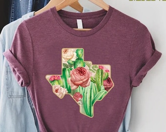 May include: A maroon t-shirt with a floral design of a cactus and roses in the shape of the state of Texas.