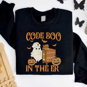 May include: Black sweatshirt with a white ghost wearing a nurse's hat and holding a medical cart. The text "CODE BOO IN THE ER" is printed on the shirt with orange pumpkins and bats.