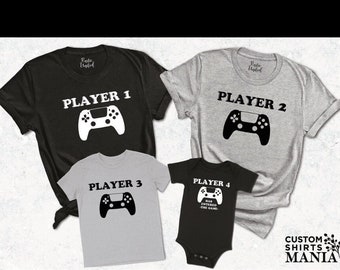 以下が含まれることがあります： 「Player 1」、「Player 2」、「Player 3」、「Player 4」の文字とビデオゲームコントローラーのグラフィックがプリントされた、グレーとブラックのTシャツ4枚。Tシャツは、一番大きいものが一番上に、一番小さいものが一番下に配置されたファミリーセットになっています。