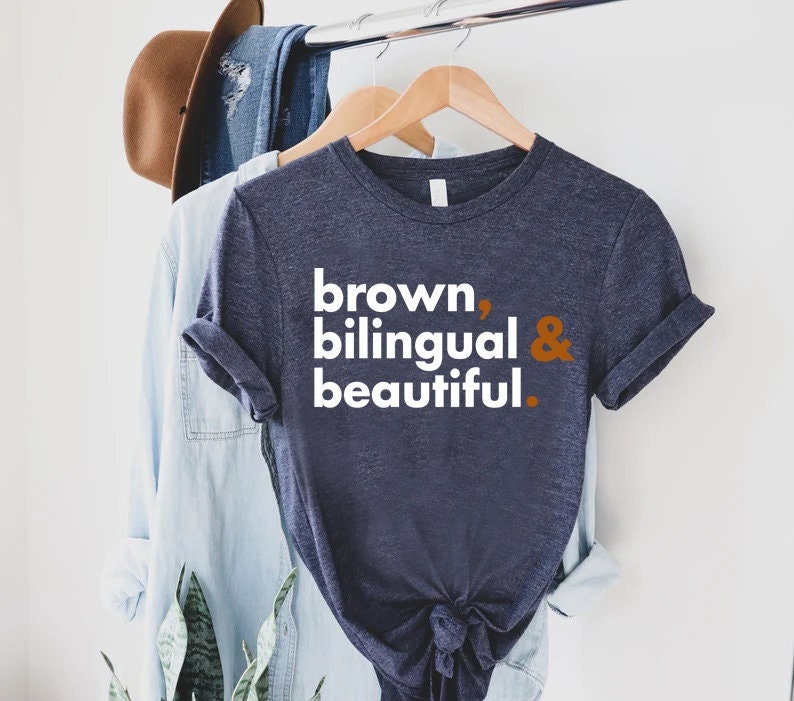 Puede incluir: Una camiseta azul marino con el texto "brown, bilingual & beautiful." impreso en blanco. La ampersand es de color naranja quemado.
