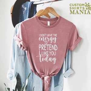 May include: A pink t-shirt with the text "I don't have the energy to pretend I like you today" in white lettering.