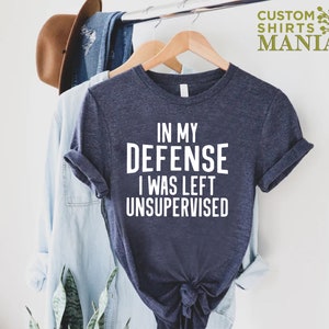 May include: A navy blue t-shirt with white text that reads "In my defense I was left unsupervised".