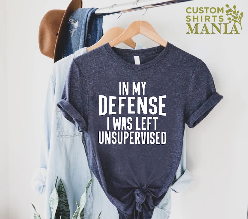 May include: A navy blue t-shirt with white text that reads "In my defense I was left unsupervised".