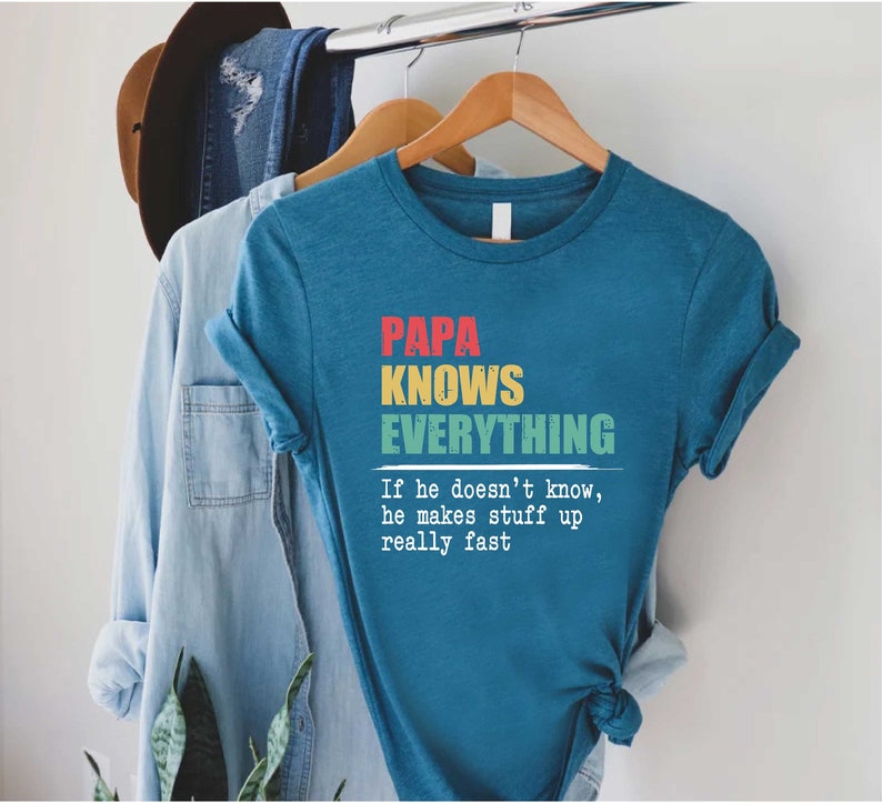 May include: Teal t-shirt with the text "PAPA KNOWS EVERYTHING" in red, yellow, and green. Below the text is the quote, "If he doesn't know, he makes stuff up really fast."