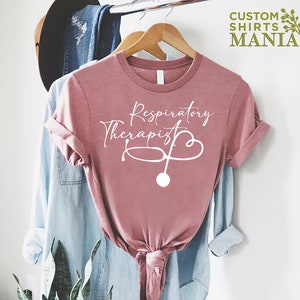 May include: A pink t-shirt with the text "Respiratory Therapist" in white cursive lettering and a stethoscope graphic.