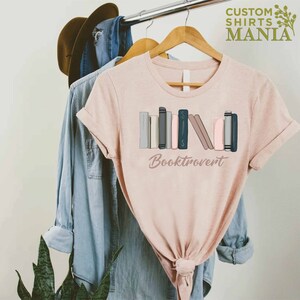 May include: A pink t-shirt with a graphic of a stack of books and the text "Booktrovert".
