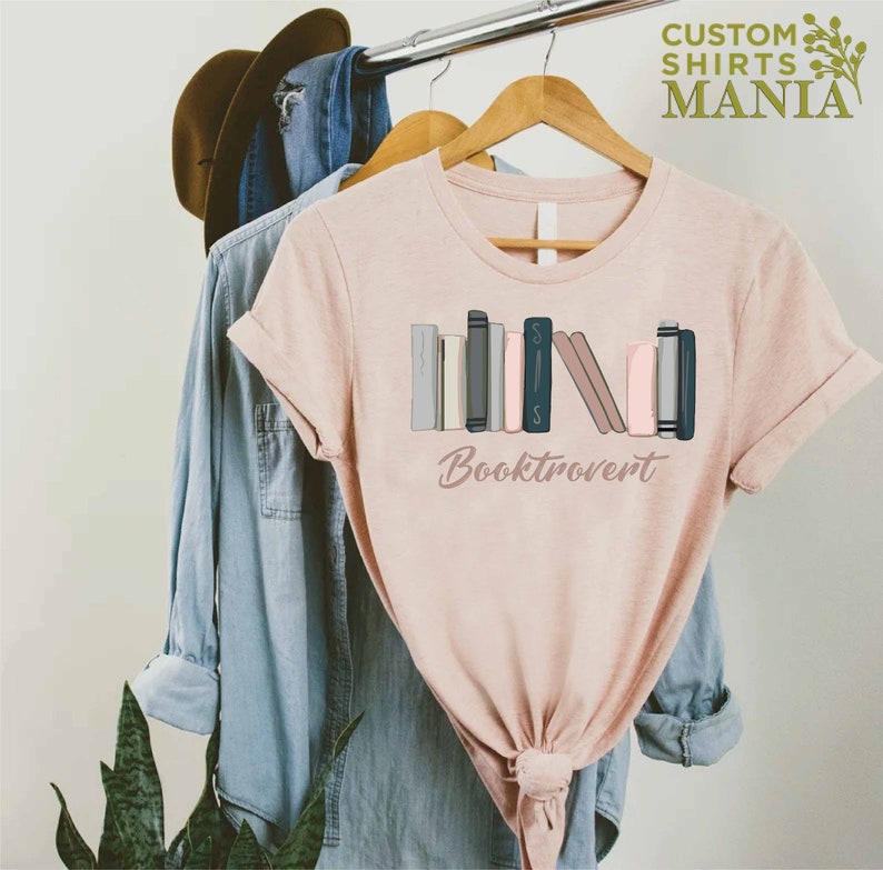May include: A pink t-shirt with a graphic of a stack of books and the text "Booktrovert".