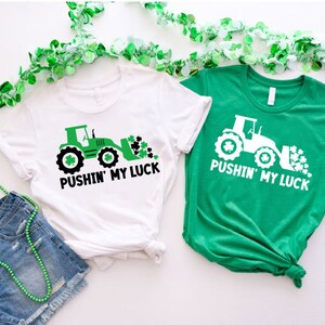 May include: Two t-shirts with a green tractor design and the text "Pushin' My Luck". The shirts are white and green.