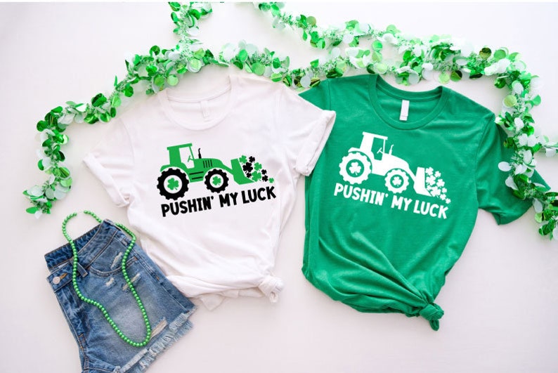May include: Two t-shirts with a green tractor design and the text "Pushin' My Luck". The shirts are white and green.