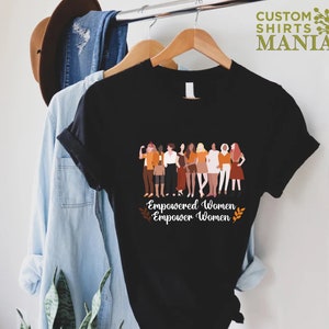 May include: Black t-shirt featuring a graphic of a group of diverse women standing together. The text "Empowered Women Empower Women" is printed below the graphic.