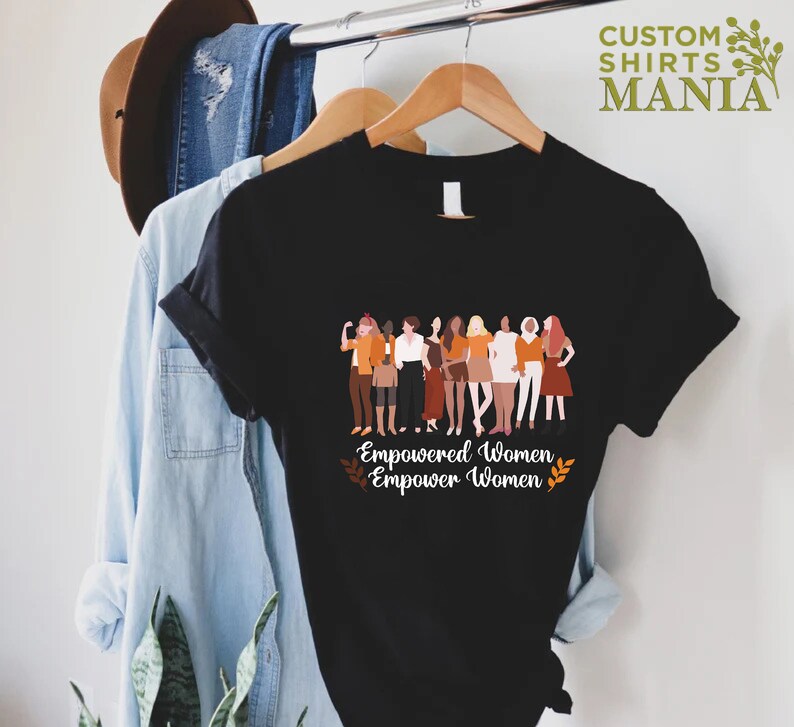 May include: Black t-shirt featuring a graphic of a group of diverse women standing together. The text "Empowered Women Empower Women" is printed below the graphic.