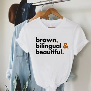 Puede incluir: Camiseta blanca con el texto "brown, bilingual & beautiful." impreso en negro y marr&oacute;n.