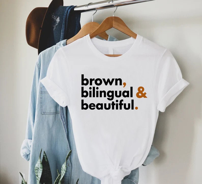 Puede incluir: Camiseta blanca con el texto "brown, bilingual & beautiful." impreso en negro y marr&oacute;n.
