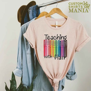 May include: A pink t-shirt with the text "Teaching with Flair" and a rainbow of colorful markers.