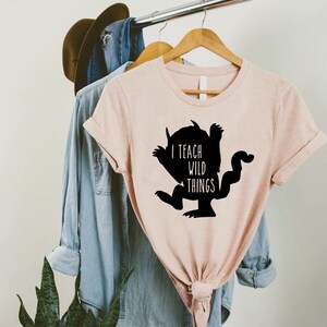 May include: A pink t-shirt with a black silhouette of a monster and the text "I teach wild things".