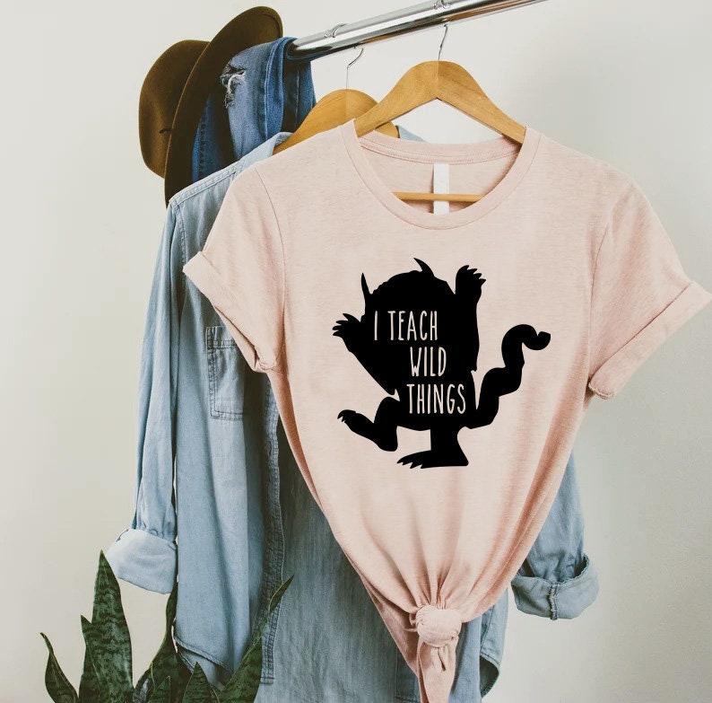 May include: A pink t-shirt with a black silhouette of a monster and the text "I teach wild things".
