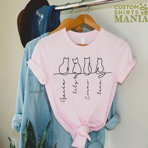 May include: Pink t-shirt with a line drawing of four cats and their names: Gracie, Lily, Cosmo, and Luna.