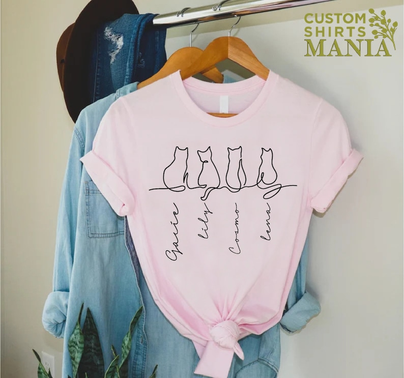 May include: Pink t-shirt with a line drawing of four cats and their names: Gracie, Lily, Cosmo, and Luna.