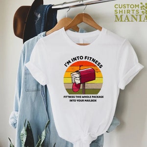 May include: White t-shirt with a vintage-style graphic of a red mailbox with the text "I'm into fitness. Fit'ness this whole package into your mailbox."