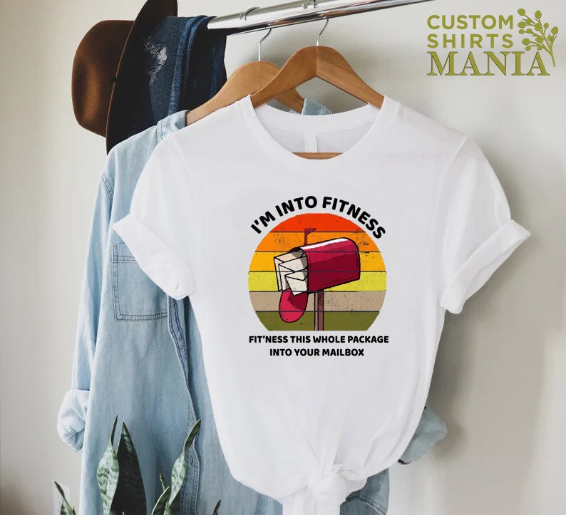 May include: White t-shirt with a vintage-style graphic of a red mailbox with the text "I'm into fitness. Fit'ness this whole package into your mailbox."