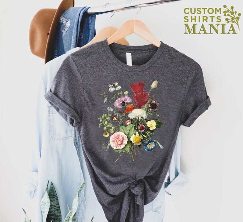 K&ouml;nnte beinhalten: Dunkelgraues T-Shirt mit einem farbenfrohen Blumenstrau&szlig;-Design. Der Strau&szlig; enth&auml;lt rosa, rote, gelbe und wei&szlig;e Blumen mit gr&uuml;nem Laub. Der Text "CUSTOM SHIRTS MANIA" ist in Gr&uuml;n oben rechts aufgedruckt.