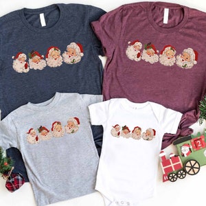 May include: A set of four t-shirts featuring a vintage-style illustration of Santa Claus's faces. The shirts are in navy blue, burgundy, gray, and white.