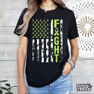 May include: Black t-shirt with a distressed American flag design featuring green ribbon symbols and the word "FIGHT" vertically down the right side.