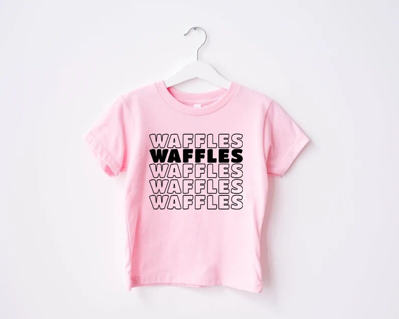 Może przedstawiać: R&oacute;żowa koszulka z kr&oacute;tkim rękawem z napisem "WAFFLES" powt&oacute;rzonym pięć razy czarnym tekstem.