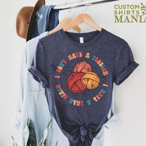 May include: A dark blue t-shirt with a colorful graphic that says "I don't have a problem I have a yarn stash". The graphic features three balls of yarn in red, orange, and yellow.