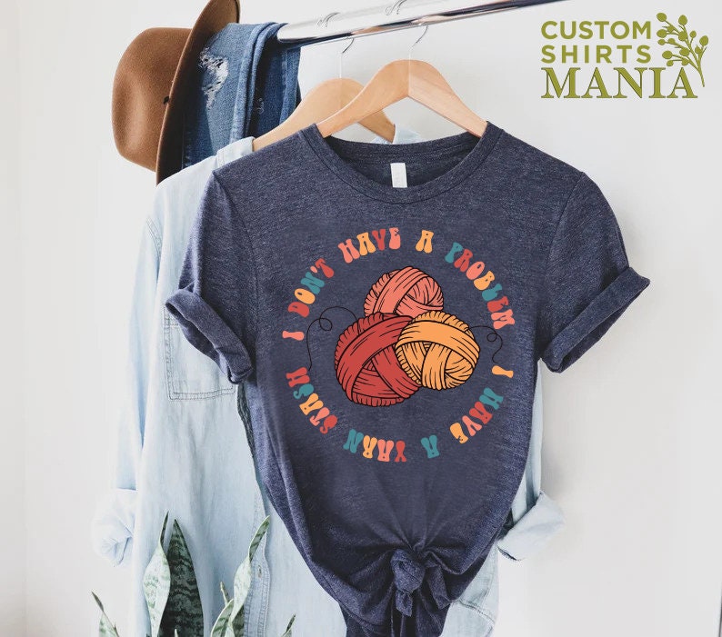 May include: A dark blue t-shirt with a colorful graphic that says "I don't have a problem I have a yarn stash". The graphic features three balls of yarn in red, orange, and yellow.