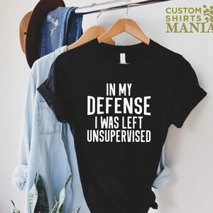 May include: Black t-shirt with white text that reads "In my defense I was left unsupervised".