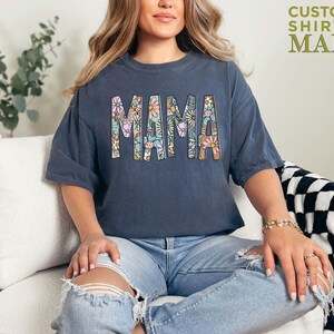 a woman sitting on a couch wearing a shirt that says mama