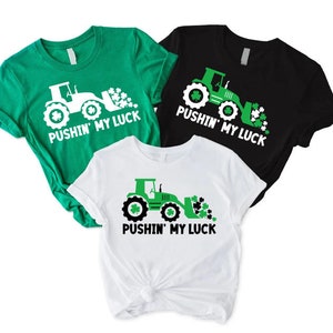 May include: Three green, white, and black t-shirts with a graphic of a green tractor with a scoop full of shamrocks and the text "Pushin' My Luck".