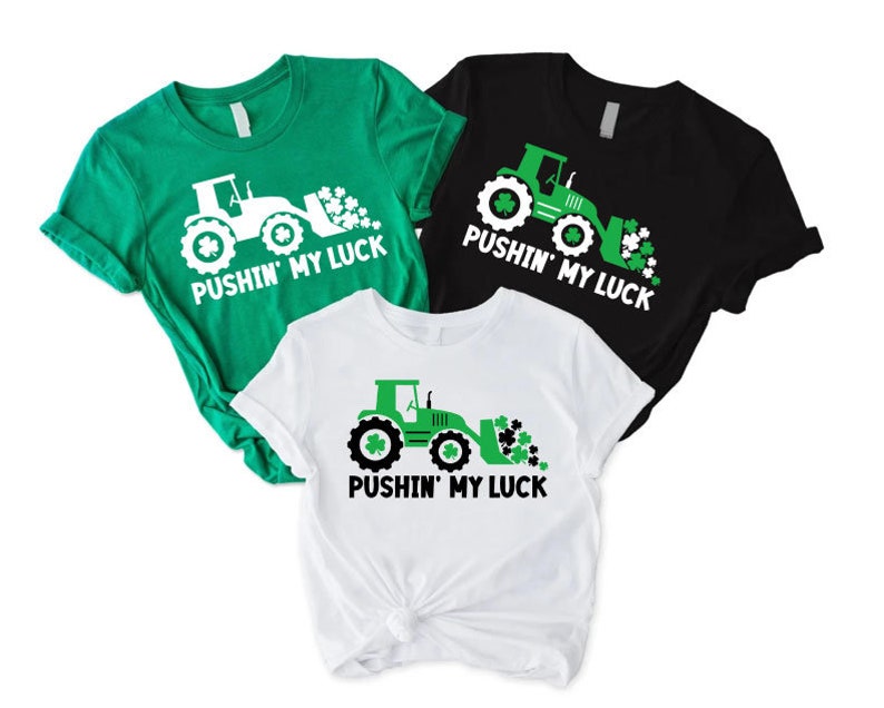 May include: Three green, white, and black t-shirts with a graphic of a green tractor with a scoop full of shamrocks and the text "Pushin' My Luck".