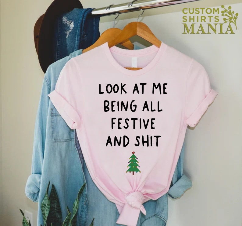 May include: Pink t-shirt with the text "Look at me being all festive and shit" and a small green Christmas tree with lights.