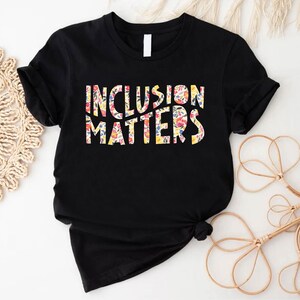 Puede incluir: Camiseta negra con el texto "Inclusion Matters" en letras blancas delineadas con un patr&oacute;n floral.